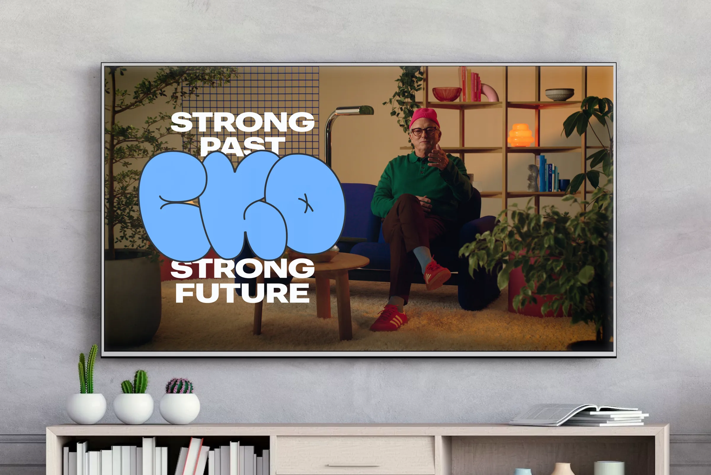 A still from the CKO hype video on a wall-mounted TV: “Strong Past, Strong Future” and the blue CKO logo over a man in a green sweater sitting in a living room.
