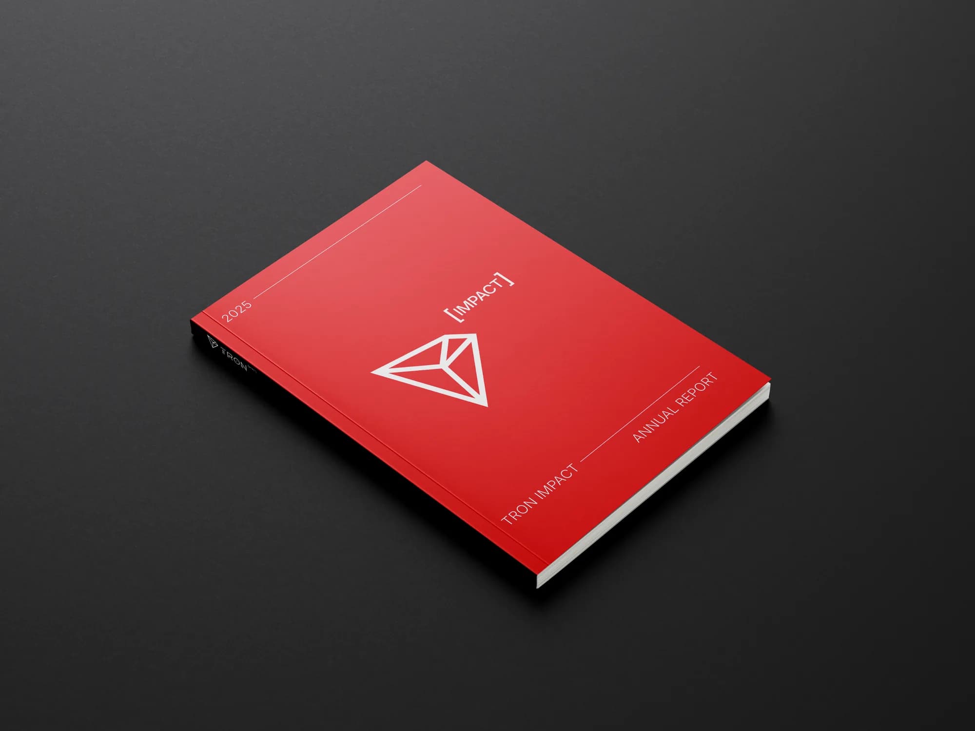 The red TRON IMPACT annual report, closed, on a dark surface.
